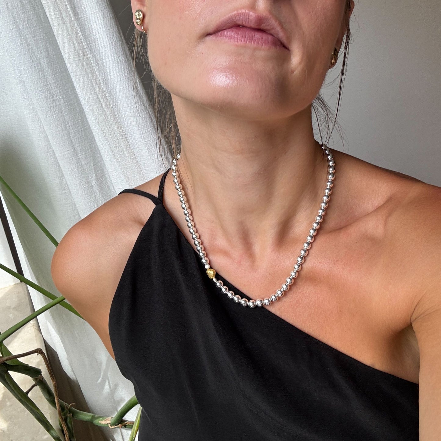 Naszyjnik z kulek hematytowych ze złotym serduszkiem na szyi modelki. A necklace of hematite beads with a gold heart on the model's neck.