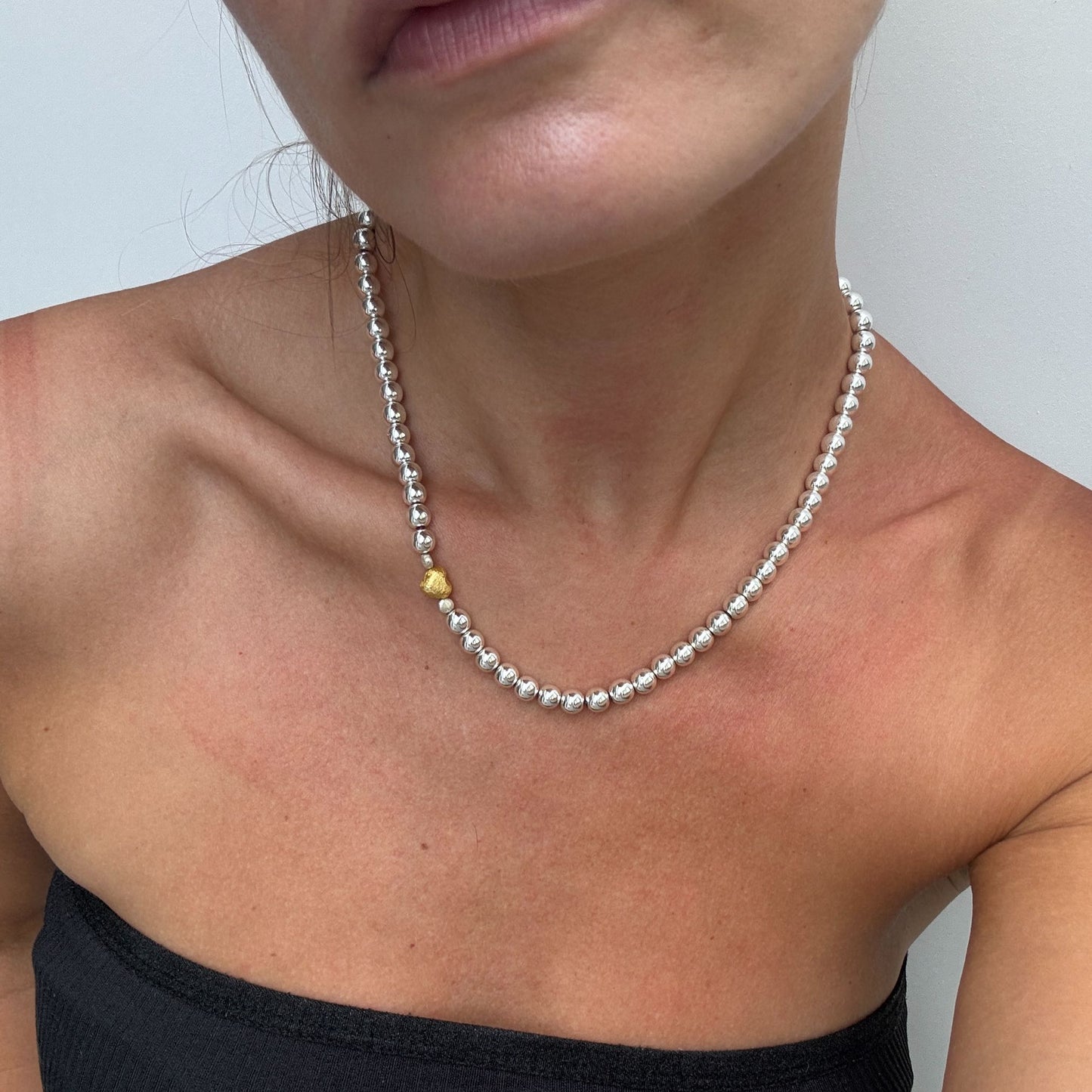 Naszyjnik z kulek hematytowych ze złotym serduszkiem na szyi modelki. A necklace of hematite beads with a gold heart on the model's neck.