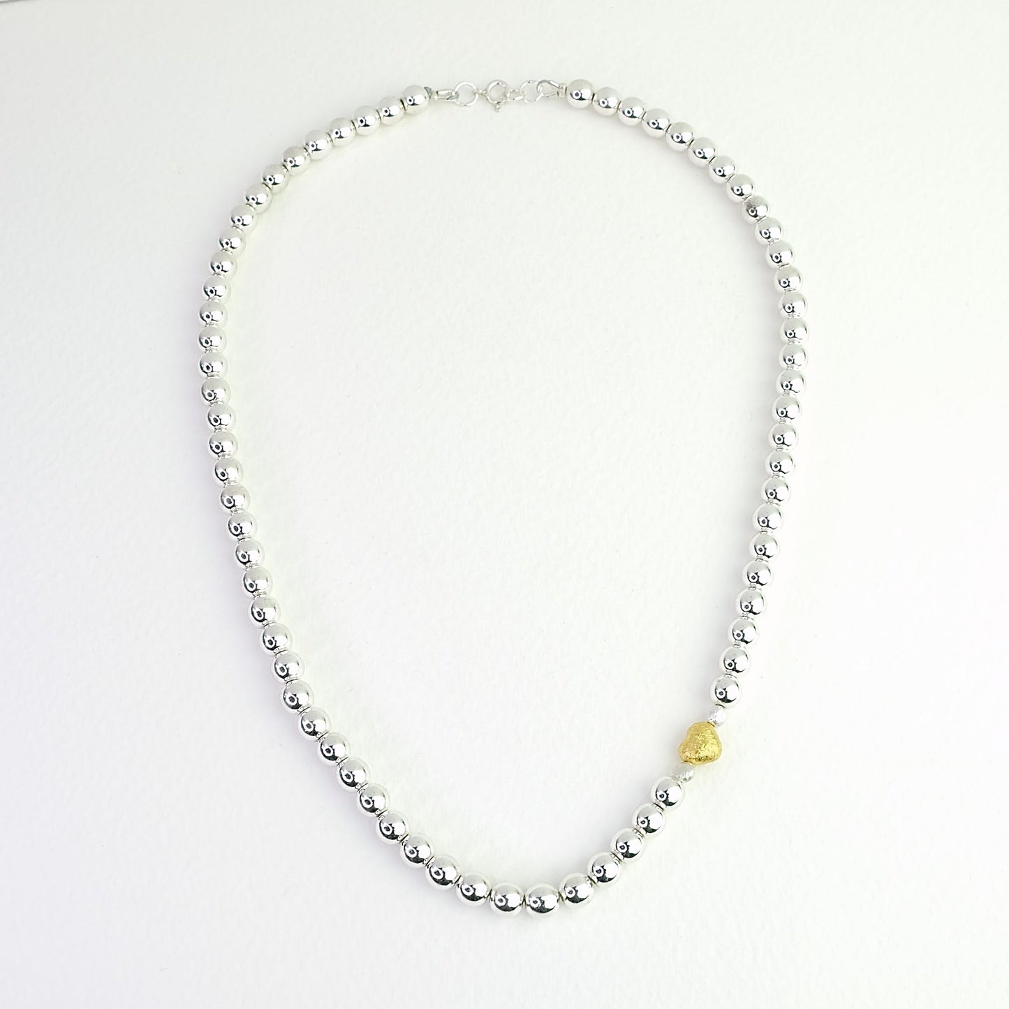 Naszyjnik z kulek hematytowych ze złotym serduszkiem na jasnym tle. A necklace of hematite beads with a gold heart on a light background.