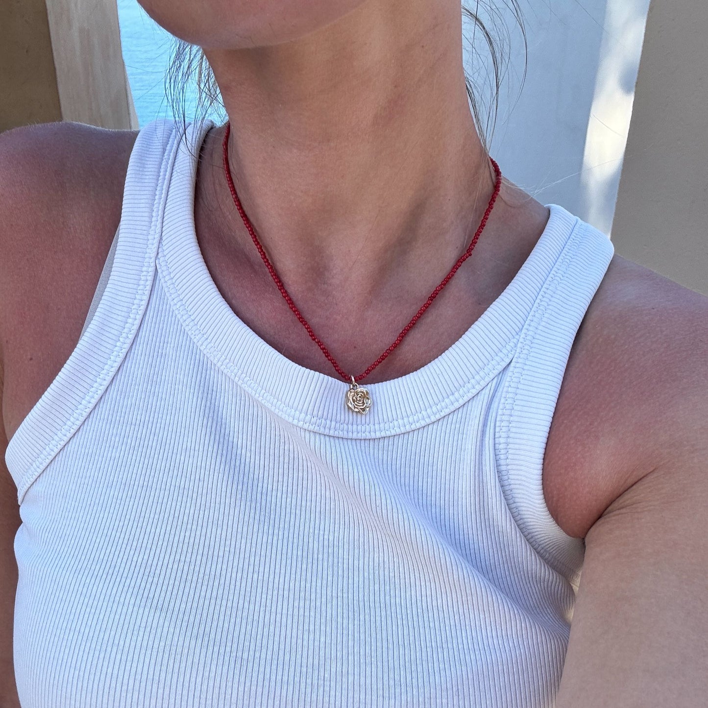 Naszyjnik z korala z zawieszką - złota róża na szyi modelki w białym tank topie. Coral necklace with a pendant - a gold rose on the neck of a model wearing a white tank top.