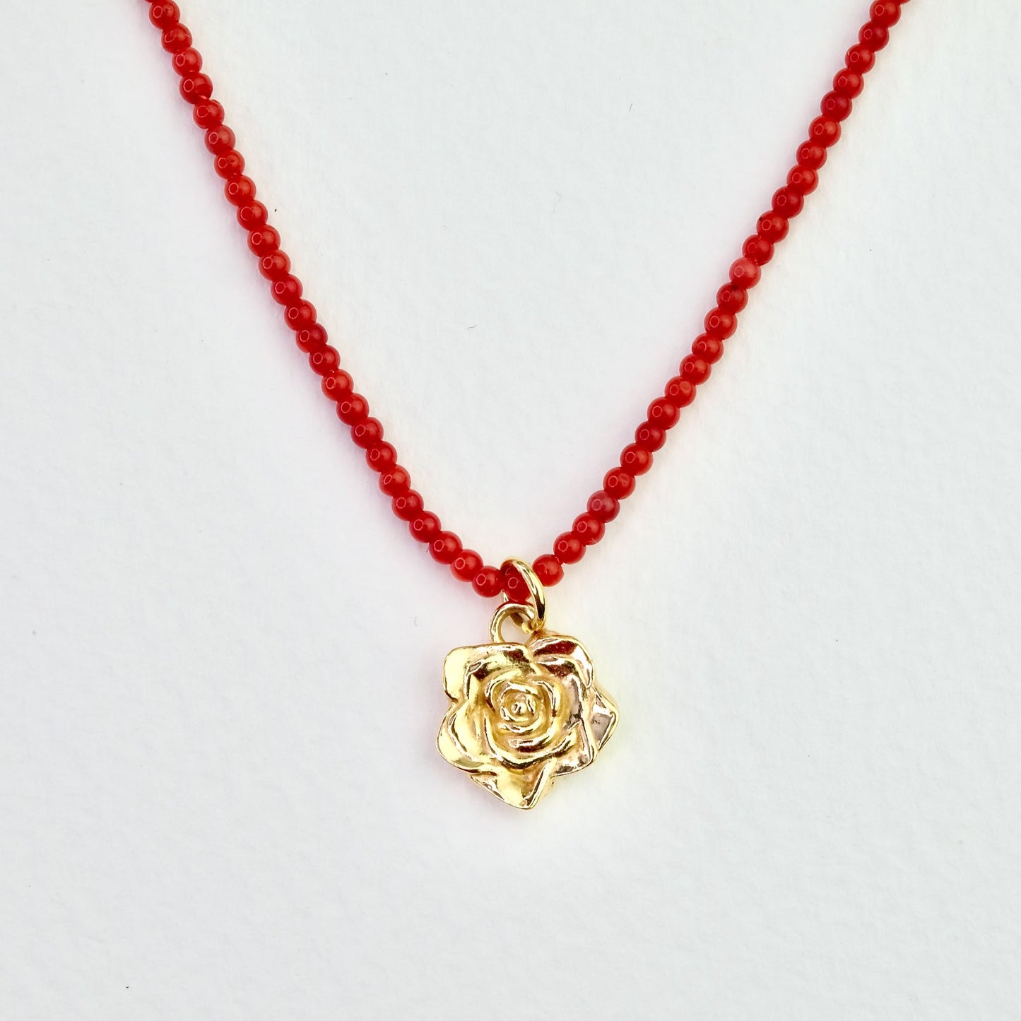 Naszyjnik z korala z zawieszką - złota róża na jasnym tle, zbliżenie. Coral necklace with a pendant - a gold rose on a light background, close-up.