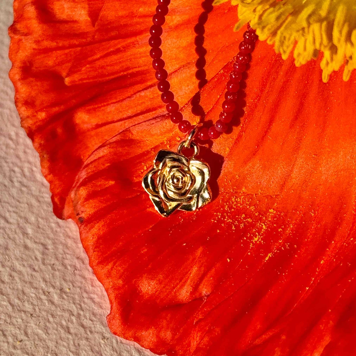 Naszyjnik z korala z zawieszką - złota róża na tle czerwonego kwiata. Coral necklace with a pendant - a gold rose against a red flower background.