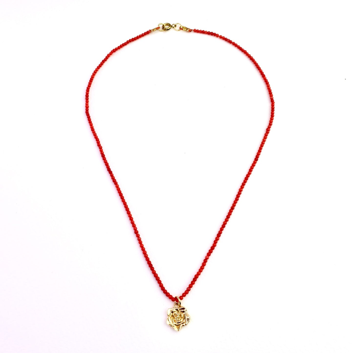 Naszyjnik z korala z zawieszką - złota róża na jasnym tle. Coral necklace with a pendant - a gold rose on a light background.