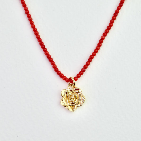 Naszyjnik z korala z zawieszką - złota róża na jasnym tle, zbliżenie. Coral necklace with a pendant - a gold rose on a light background, close-up.